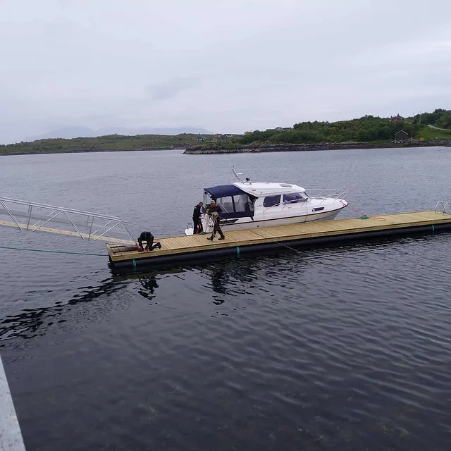 Lang flytebrygge med båt fortøyd, landgang til kai på venstre side.