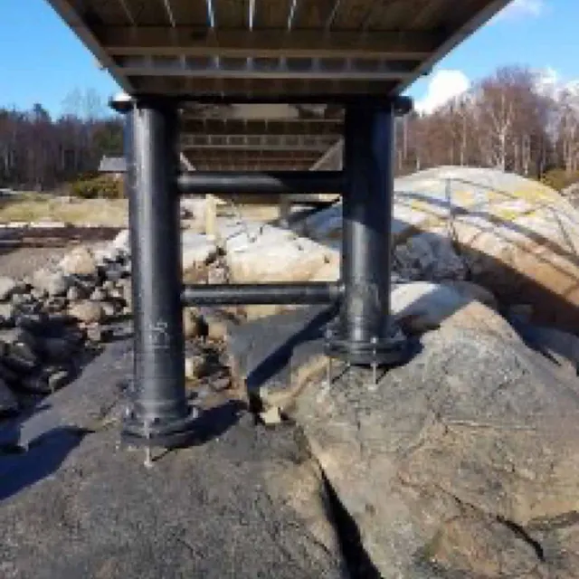 Landgang støttet av sorte stolper og bjelker, montert på svaberg.