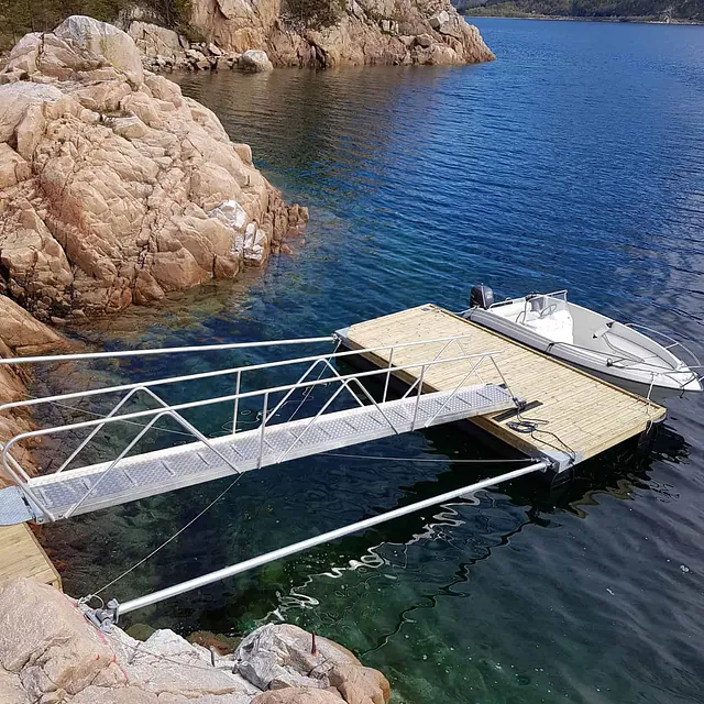 Flytebrygge ved bratte fjellvegger og klart vann, liten båt fortøyd.