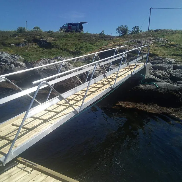 Landgang fra brygge opp til svaberg med gresskledd topp.