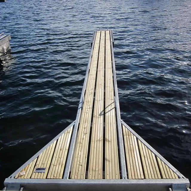Smal trebrygge strekker seg ut i vannet med vinterlandskap i bakgrunnen.