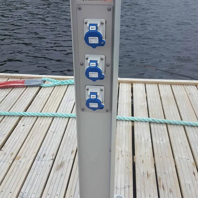 Strømsøyle med blå stikkontakter står montert på trebrygge ved vann.
