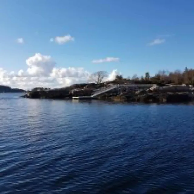 Lang landgang fra brygge til land sett fra sjøen på solskinnsdag.