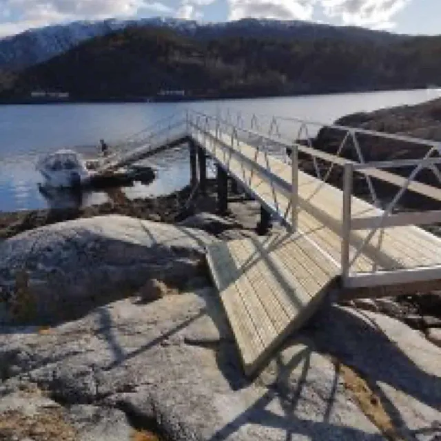 Landgang med rekkverk som går fra brygge til svaberg ved vannet.